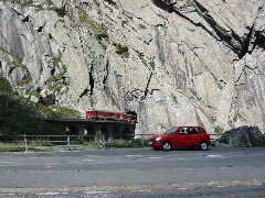 Zwei mehr oder weniger kleine, rote Fahrzeuge in der Schöllenen-Schlucht